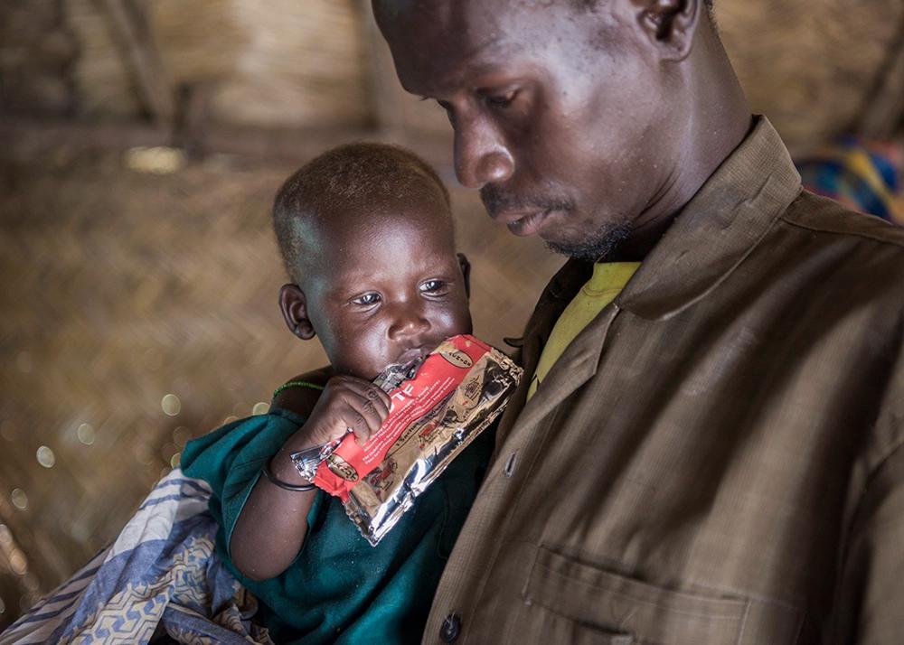 Man med litet undernärt barn i famnen som äter nötkräm